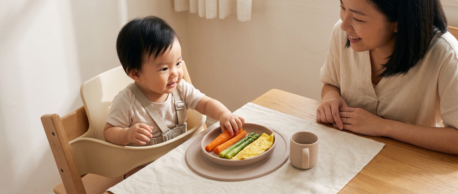 A baby seated in a high chair with a parent beside a plate of food.